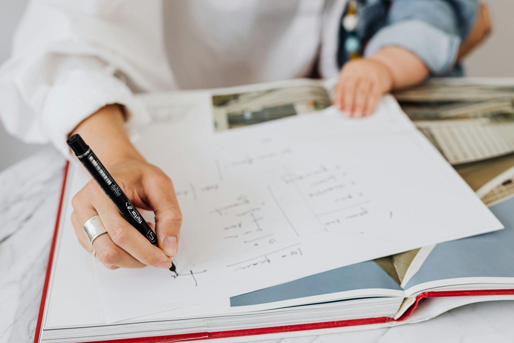A detailed shot of a hand writing on paper next to a book, with a child nearby.