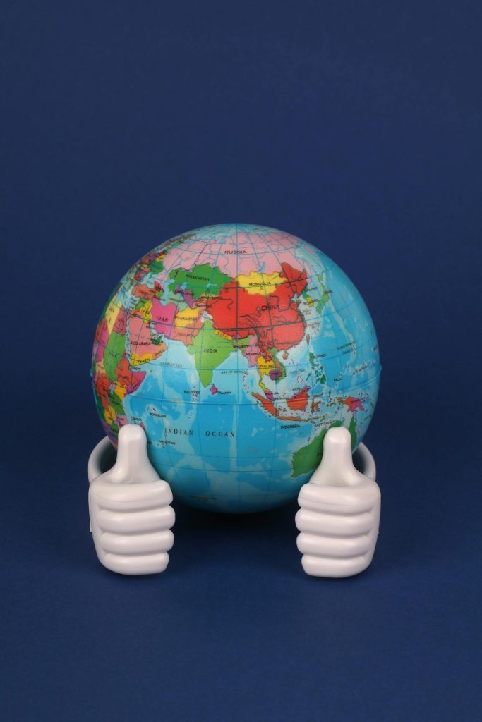 A globe with colorful continents held by ceramic thumbs against a dark background.