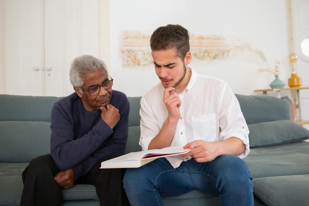 Young man and senior discussing a book at home, fostering intergenerational connection.