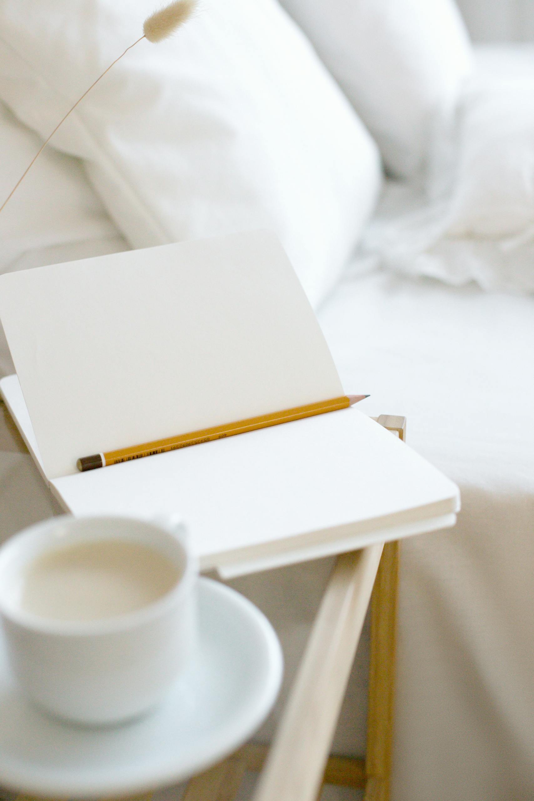 A minimalist home workspace featuring an open notebook and pencil with coffee on a wooden tray.