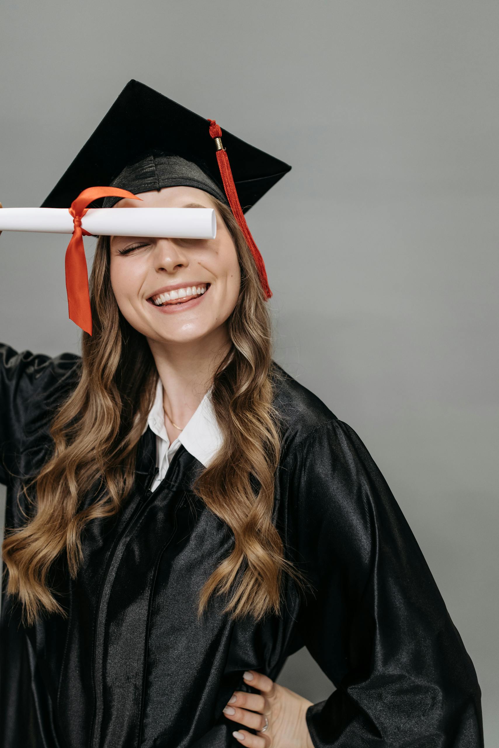 Smiling woman in graduation gown celebrating with diploma in hand indoors.