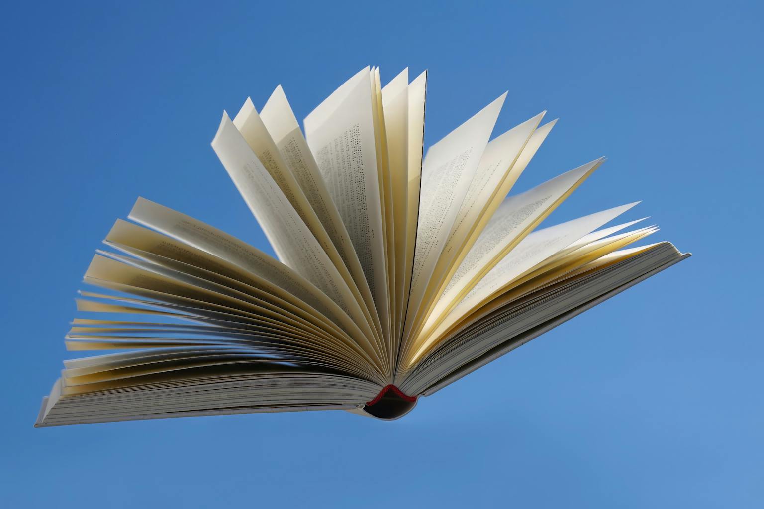 An open book with pages fanned out, floating against a bright blue sky, symbolizing imagination and knowledge.